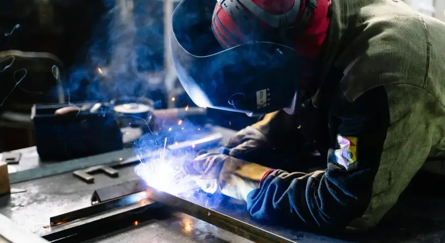 Saldatore al lavoro, scintille luminose e fumo blu avvolgono la tempra dell'acciaio inox.