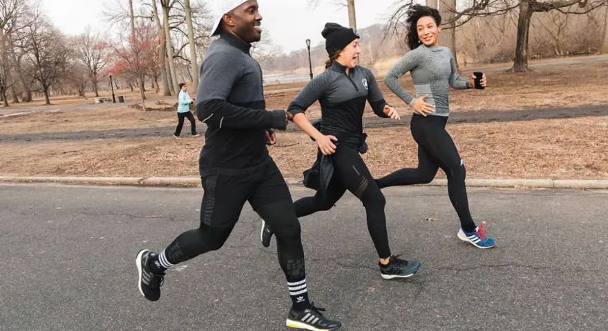 Tre amici corrono in un parco in inverno, mostrando come vestirsi per correre in questa stagione con abbigliamento tecnico.