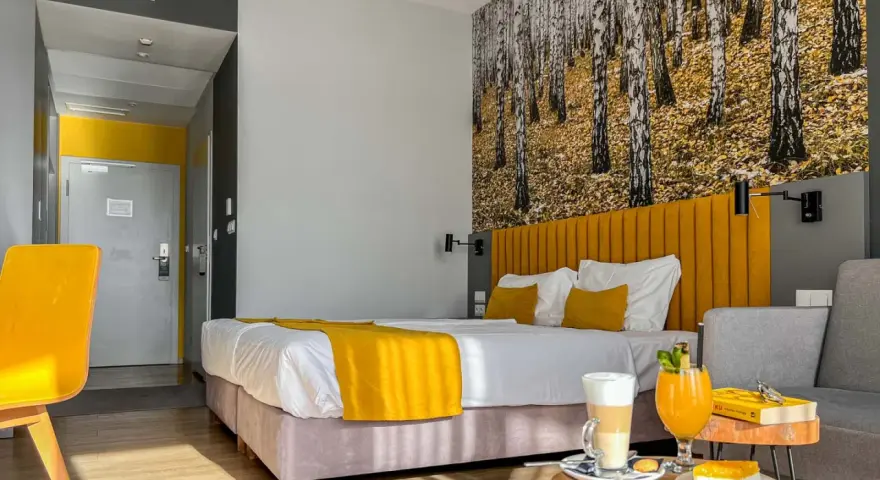 Pokój hotelowy z motywem lasu, żółtym akcentem i napojami. Idealne miejsce na relaks, jak sugerują notera hotel spa opinie.