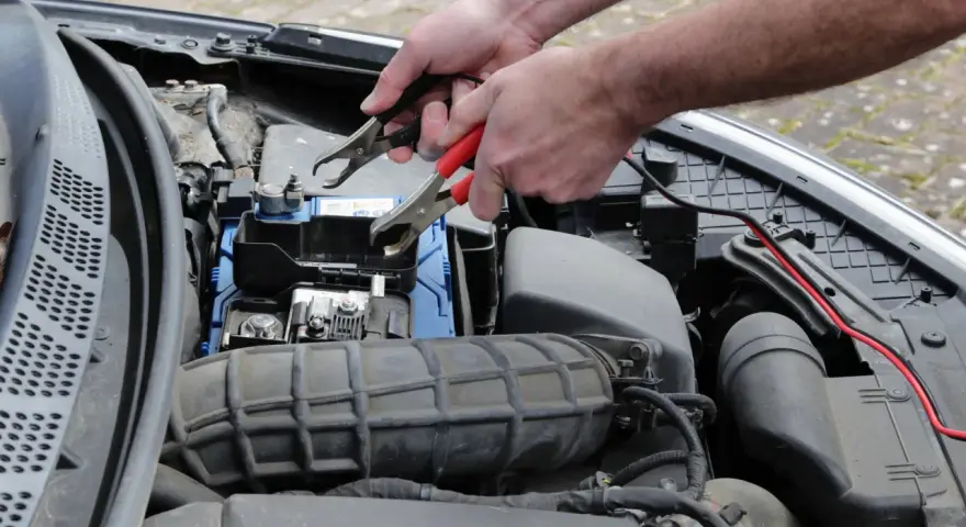 Ręce podłączają kable do akumulatora, bo auto nie odpala.