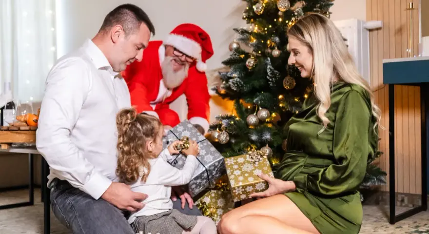 Rodzina otwiera prezenty przy choince, a Mikołaj uśmiecha się w tle. Wesołe święta w hotelu.