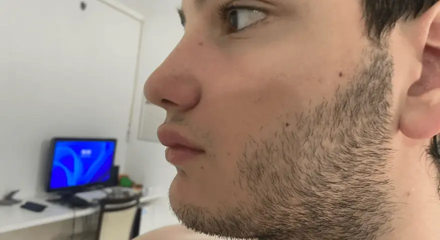 Perfil de un joven con barba incipiente, preparándose para afeitar barba. Al fondo, un monitor con pantalla azul.
