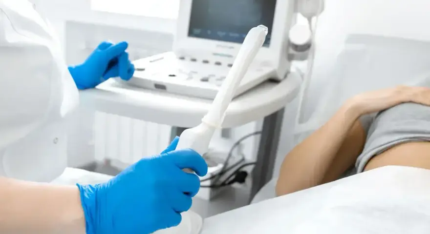 Lekarz w niebieskich rękawiczkach trzyma sondę USG, przygotowując się do badania. Na ekranie widoczne są prawidłowe wymiary macicy w usg.