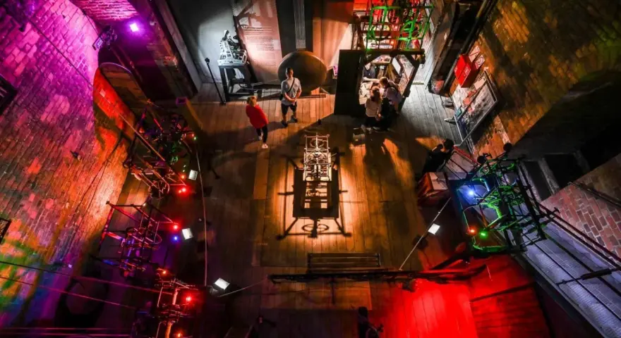 W muzeum nauki gdańskiej zwiedzający podziwiają mechanizmy i eksponaty. Kolorowe światła podkreślają atmosferę.