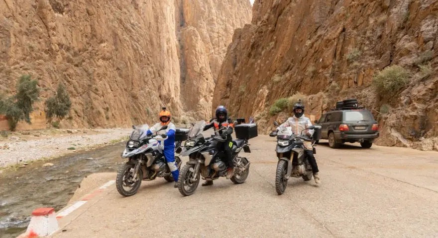 Tre moto e un fuoristrada pronti per avventurosi itinerari in moto in Marocco, tra canyon mozzafiato e un fiume.