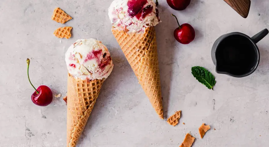 Zwei Waffelhörnchen mit Joghurt Kirsch Eis, garniert mit frischen Kirschen und Minze.
