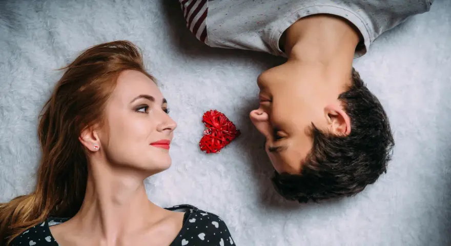 Para leży obok siebie, patrząc na siebie z dystansem, jakby odczuwali niedopasowanie seksualne. Między nimi leży czerwone serce.