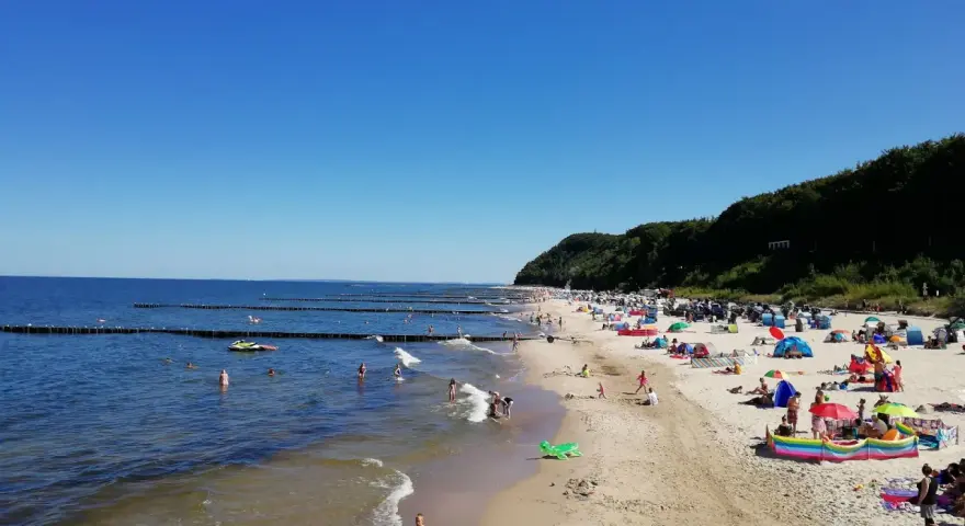 Sonniger Tag am Strand Koserow mit vielen Badegästen, bunten Sonnenschirmen und spielenden Kindern im flachen Wasser.