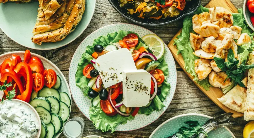 Pyszny grecki posiłek: pieczona ryba, sałatka grecka, kurczak, hummus i ciasto filo, które ma dużo węglowodanów.