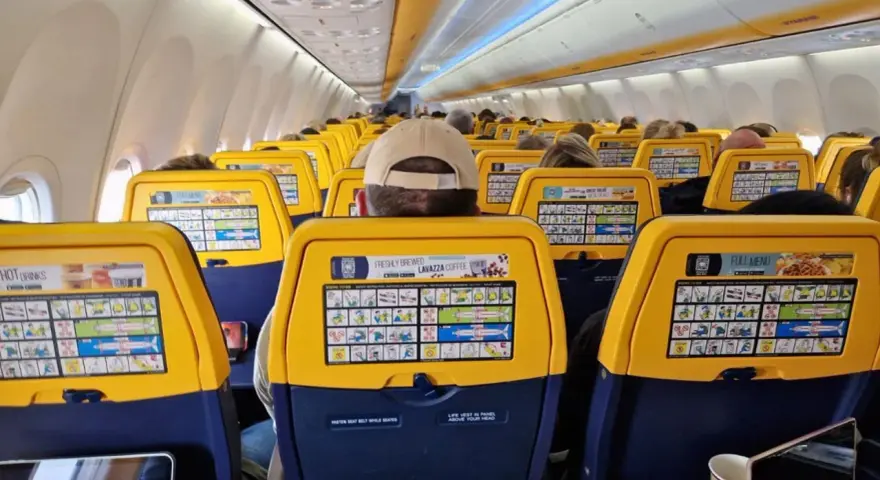 Widok wnętrza samolotu Ryanair z żółtymi oparciami siedzeń i instrukcjami bezpieczeństwa.