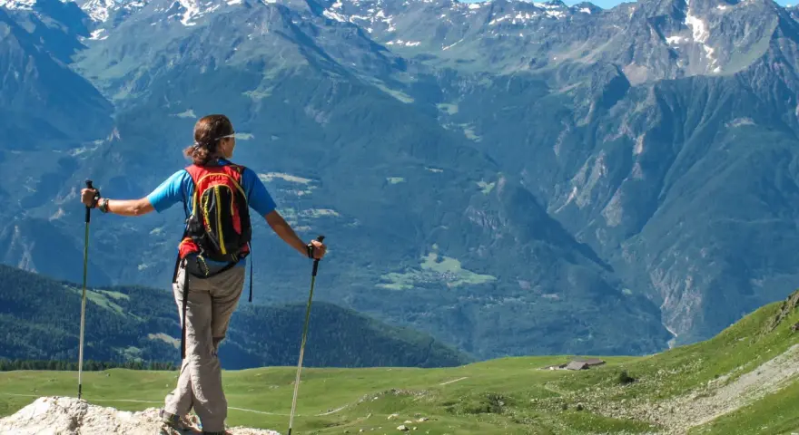 Donna con zaino e bastoncini da trekking ammira i maestosi **sentieri Valle d'Aosta** e le cime innevate.