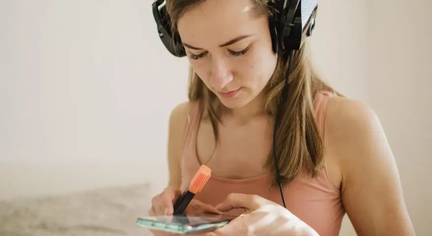 Dziewczyna w słuchawkach przegląda spotify lyrics na telefonie, zaznaczając fragmenty pomarańczowym pisakiem.