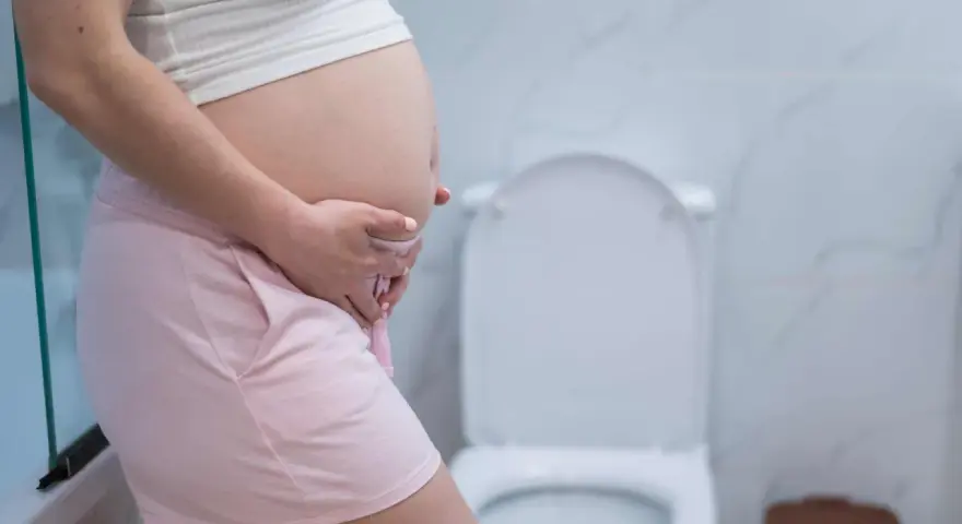 Ciąża to piękny czas, ale czasem pojawia się popuszczanie moczu. Kobieta w ciąży w łazience, obok toalety.