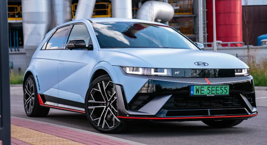 Jasnoniebieski Hyundai IONIQ 5 N z czarnymi akcentami i czerwonymi detalami, zaparkowany przed przemysłową instalacją.