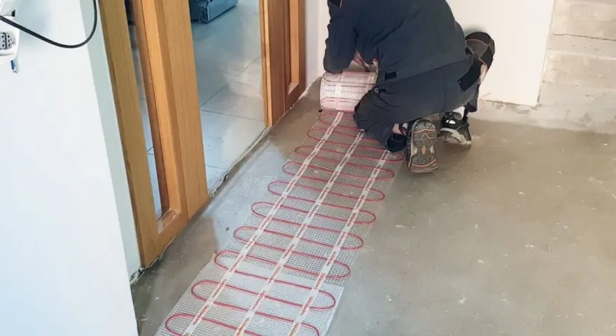 Instalator montuje matę grzewczą, przygotowując ogrzewanie elektryczne podłogi.