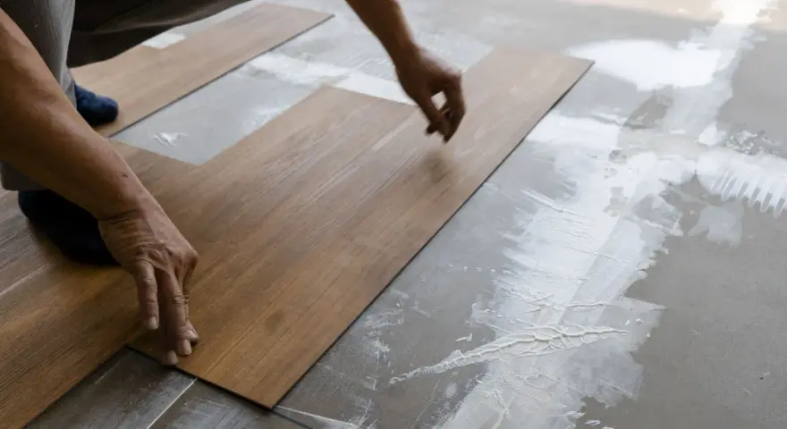 Hände legen Holzoptik-Vinylboden auf Kleber. Das Verlegen von Vinylboden erfordert Präzision.