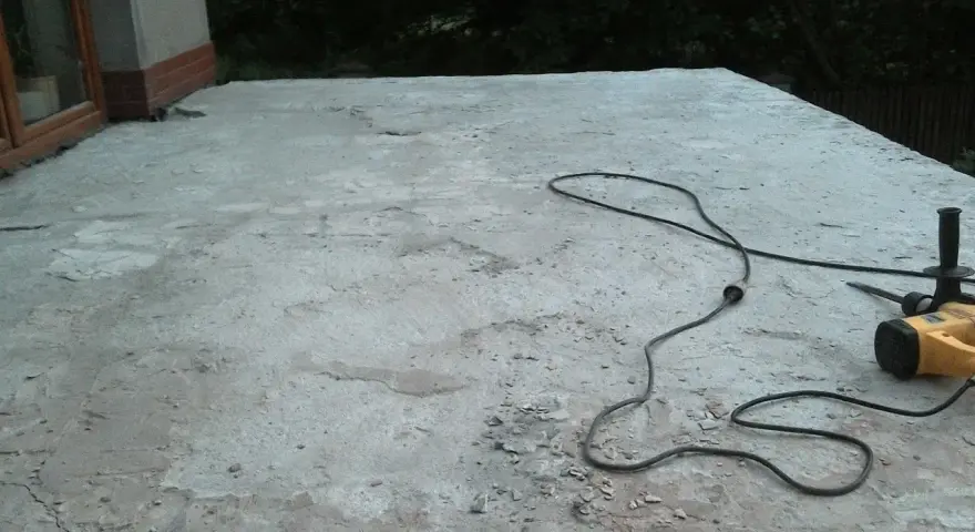 Betonowy taras czeka na remont. Obok leży młot udarowy, gotowy do pracy. Nivoplan pomoże w pracach.