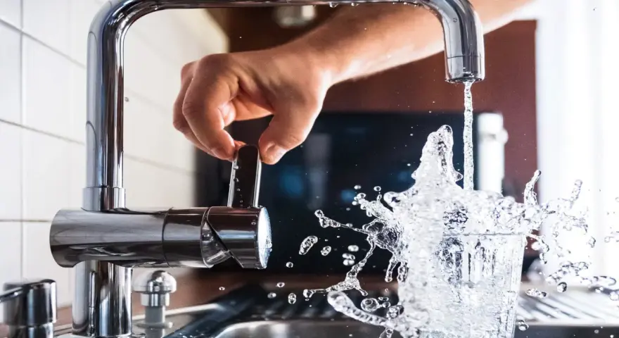 Mano girando la llave para cuidar el agua, que salpica al llenar un vaso.