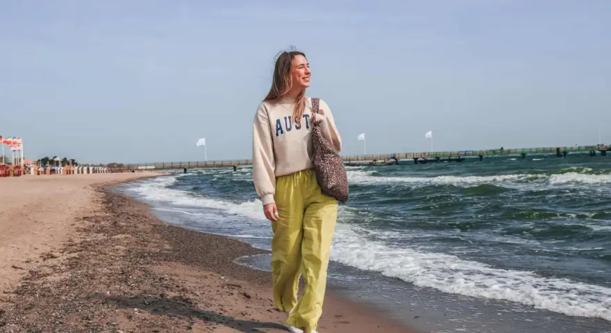 Frau spaziert am stein strand entlang, die Wellen rauschen.