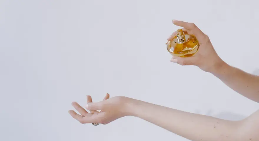 Dłoń trzymająca perfumy nad drugą dłonią.