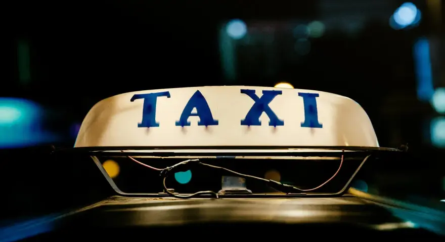 Tetto di un taxi con la scritta "TAXI" in blu. La luce soffusa e i riflessi suggeriscono la notte, un momento in cui ci si interroga quanto guadagnano i tassisti.