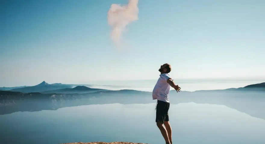 Mann mit ausgebreiteten Armen auf einem Felsvorsprung, der Rauch in den Himmel stößt. Ein Moment der Freiheit, wie Gottes Gunst.
