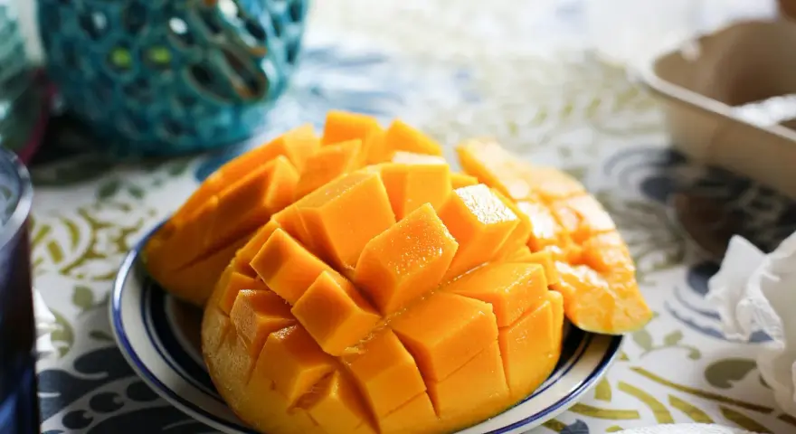 En skål med skivad mango, full av vitaminer, på en duk med mönster.