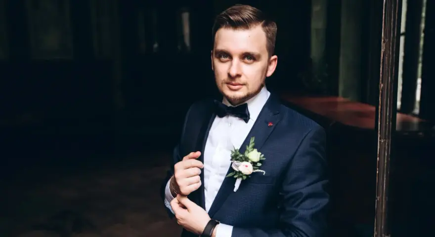 Elegancki mężczyzna w granatowym smokingu z kamizelką, z butonierką.