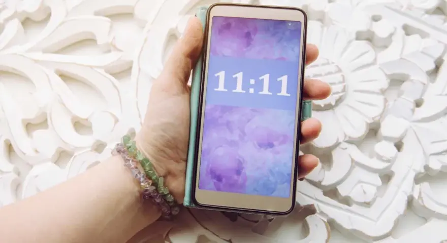 Dłoń trzyma telefon z wyświetloną godziną 11:11, co może mieć szczególne znaczenie.