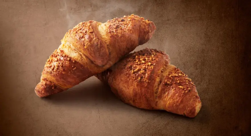 Dwa chrupiące croissanty posypane orzechami. Pyszna przekąska, ale warto pamiętać o ich kaloryczności - croissant kcal.