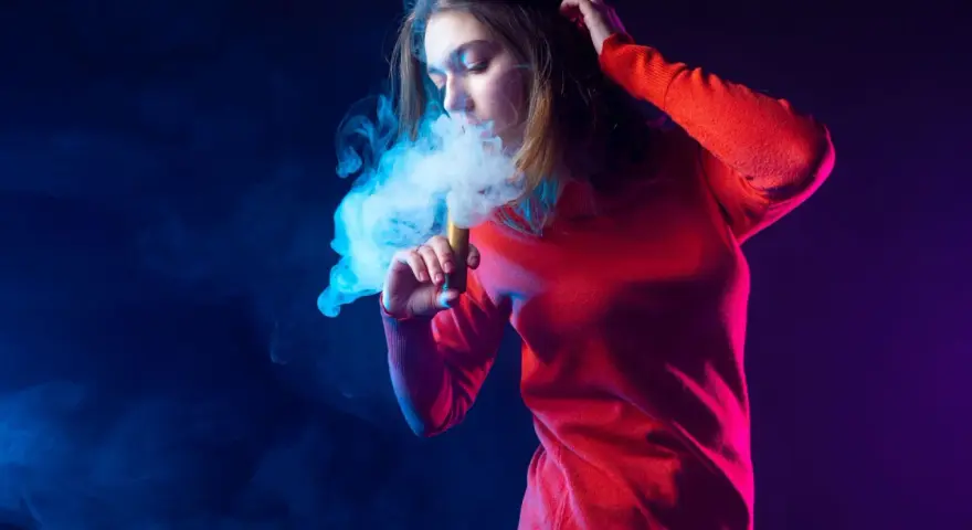 Joven exhala humo azul de un vaper. El vaper con nicotina es malo para la salud.