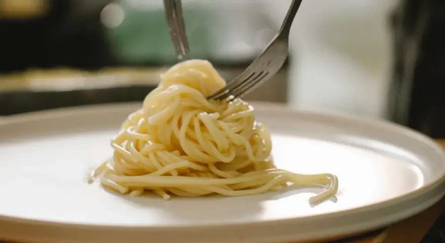 Spaghetti al limone cremosi serviti su un piatto bianco, con due forchette che li raccolgono.