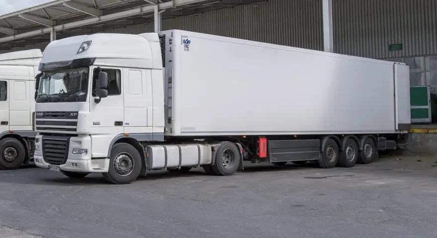 Biała naczepa chłodnicza z ciągnikiem DAF XF, gotowa do transportu.