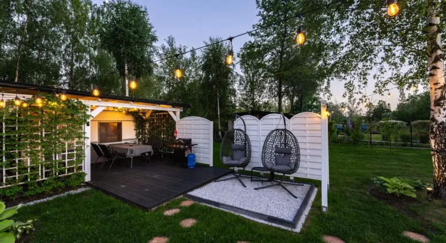 Idealne miejsce na camping w Ochabach: zadaszony taras z grillem, stolikiem i wiszącymi fotelami. Wieczorem rozświetla go girlanda żarówek.
