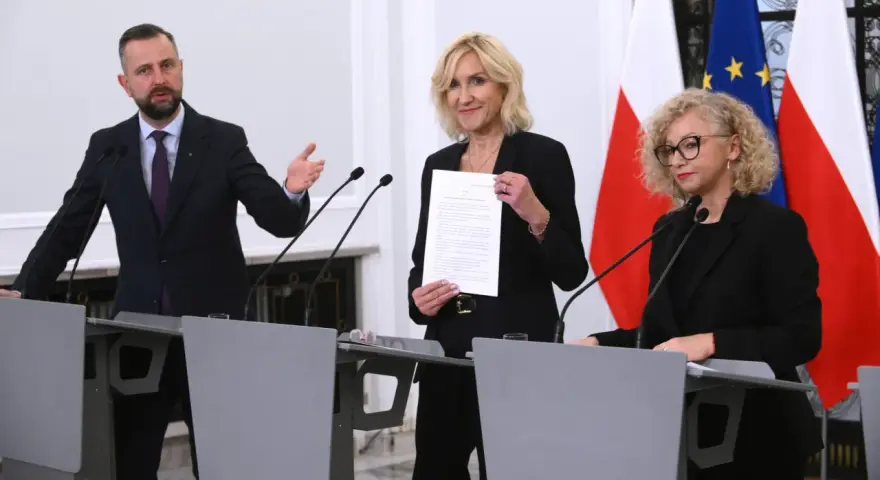 Trzy osoby przy mównicach, w tle flagi Polski i UE. Wibracja związku 8.