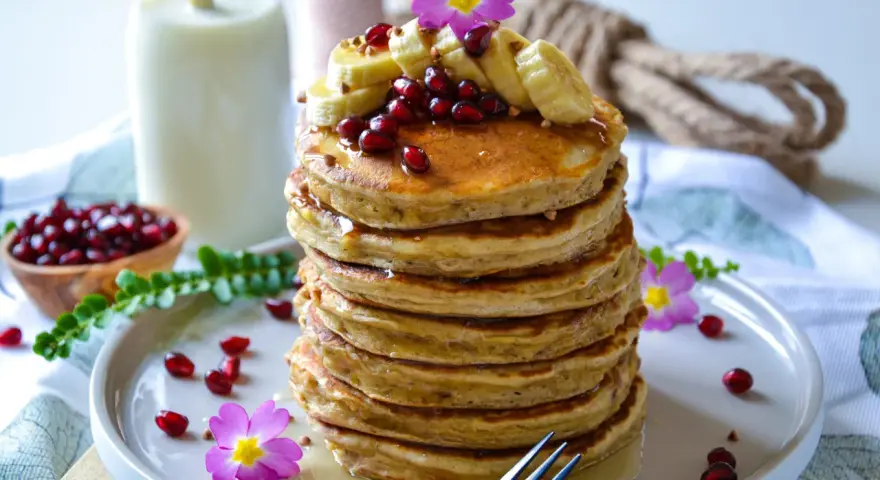 Pile de pancake banane avoine, garnie de fruits rouges, de rondelles de banane et de fleurs roses. Un délice matinal !