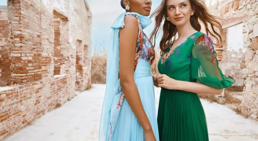 Deux femmes portent des robes élégantes, parfaites pour une tenue mariage avril. L'une est en bleu ciel plissé, l'autre en vert émeraude.