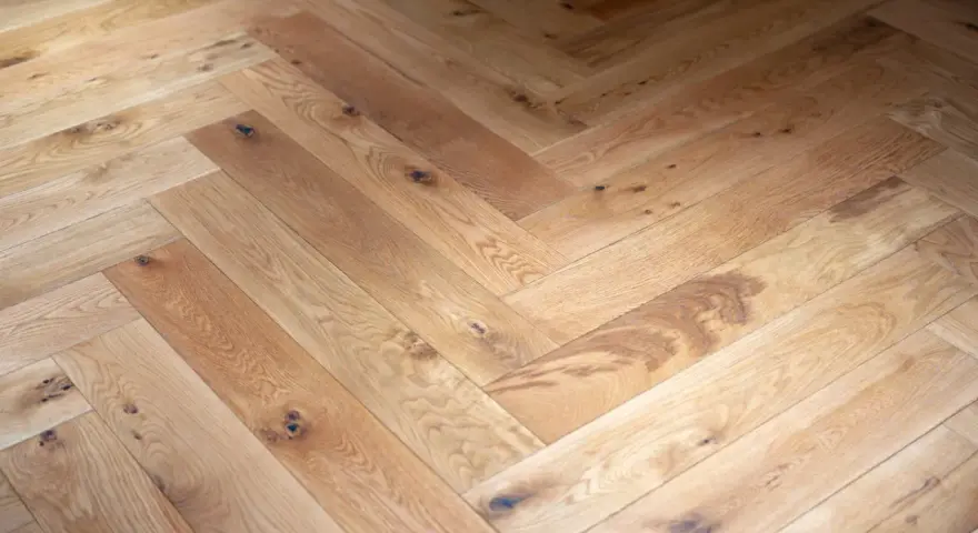 Tarima de madera en espiga, con nudos y vetas naturales, creando un patrón clásico y cálido.