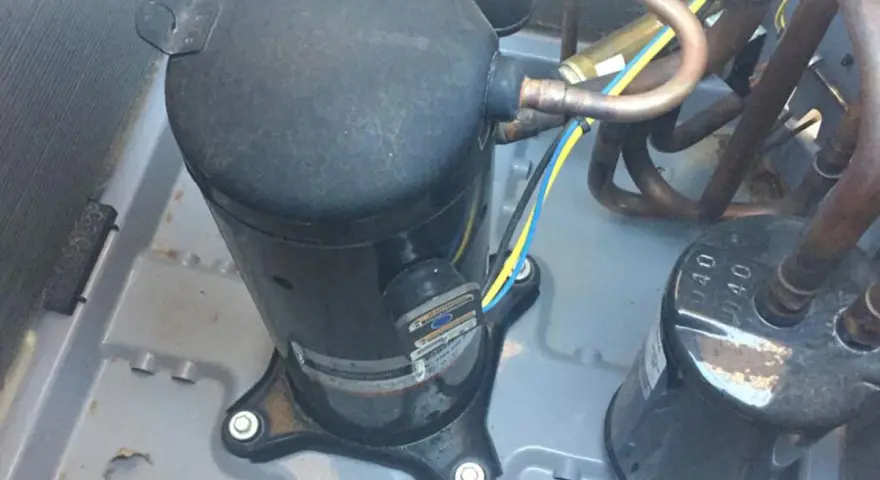 Close-up of an AC pump replacement in progress. A large black compressor sits on a gray base, connected to copper tubing and wires.