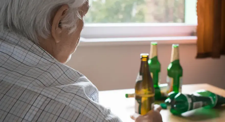 Starszy mężczyzna z butelkami piwa. Alkoholizm po 70. to trudna walka.