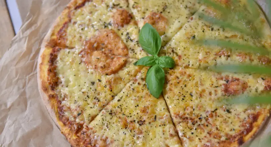 Pyszna pizza z ciągnącym się serem, posypana ziołami i udekorowana listkiem bazylii. Idealna na wspólne chwile.