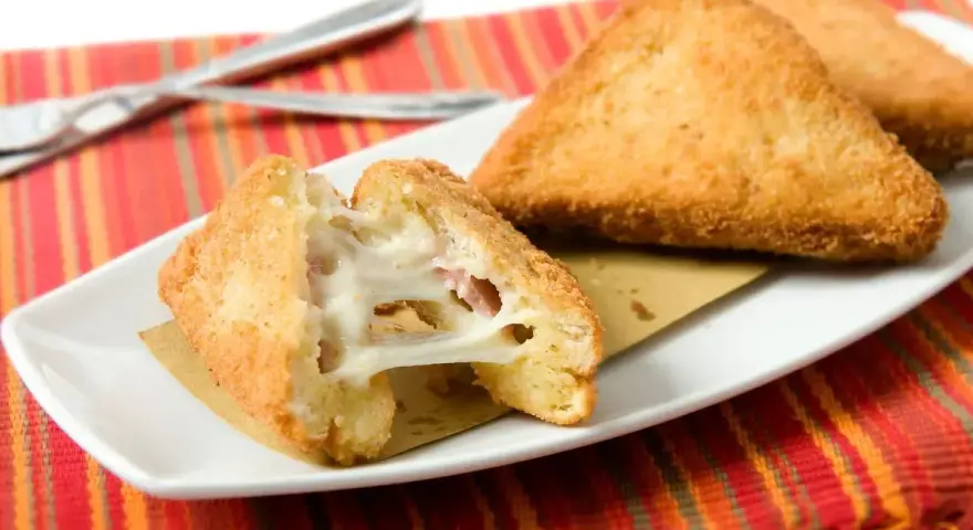 Mozzarella in carrozza dorata e filante, cotta in friggitrice ad aria, servita su un piatto bianco con tovaglietta colorata.