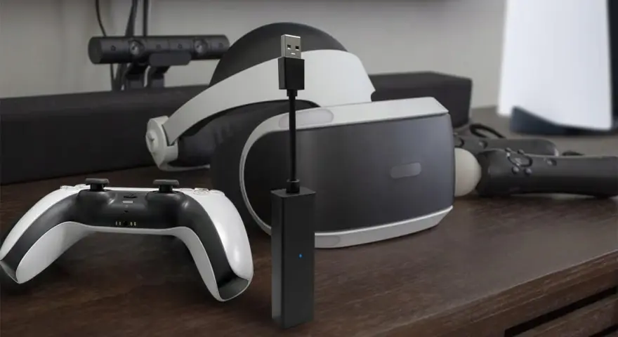 Czarny adapter PlayStation Camera z niebieską diodą, obok gogli VR i kontrolera.