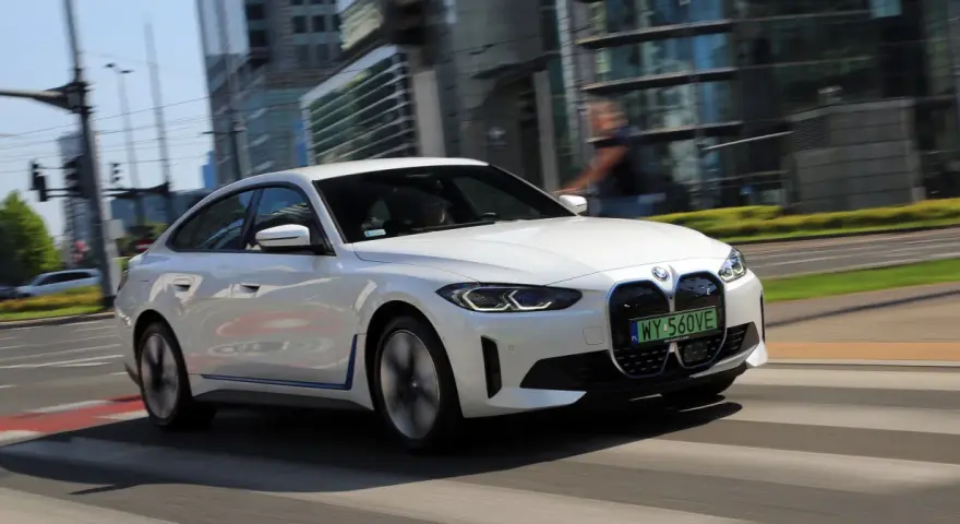 Białe BMW i4 w ruchu miejskim, z widocznymi światłami LED i grillem.