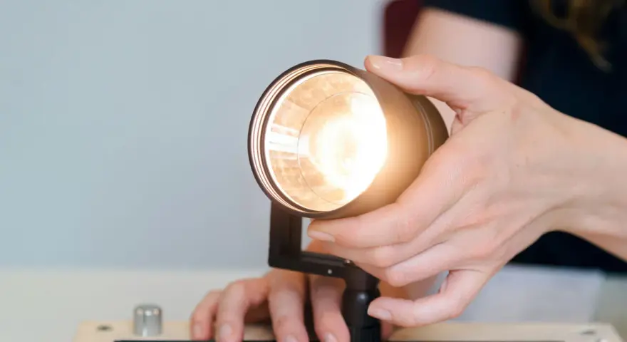 Händer justerar en lampa, kanske för att ta bort dimmer. Ljuset är starkt.