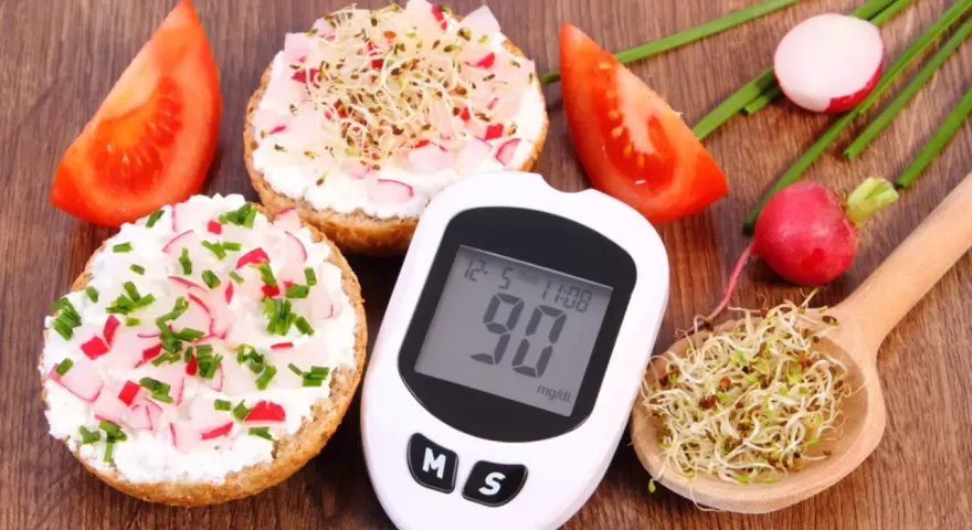 Zdrowe śniadanie dla cukrzyka: kanapki z twarożkiem, rzodkiewką i szczypiorkiem, pomidory, kiełki i glukometr pokazujący 90 mg/dl.