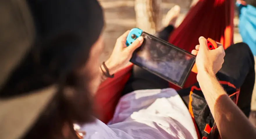 Osoba w hamaku gra na Nintendo Switch. Czas ładowania konsoli jest krótki, więc można grać wszędzie.