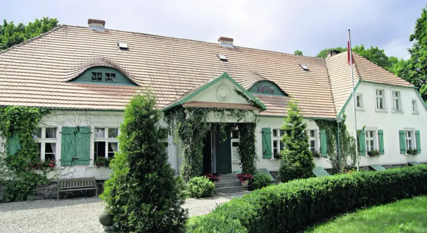 Urokliwy dwór Wybickich z zielonymi okiennicami i pnączami.