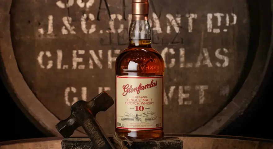 Glenfarclas 10YO, idealny wybór do rankingu top 10 whisky. Butelka na tle beczki z destylarni.