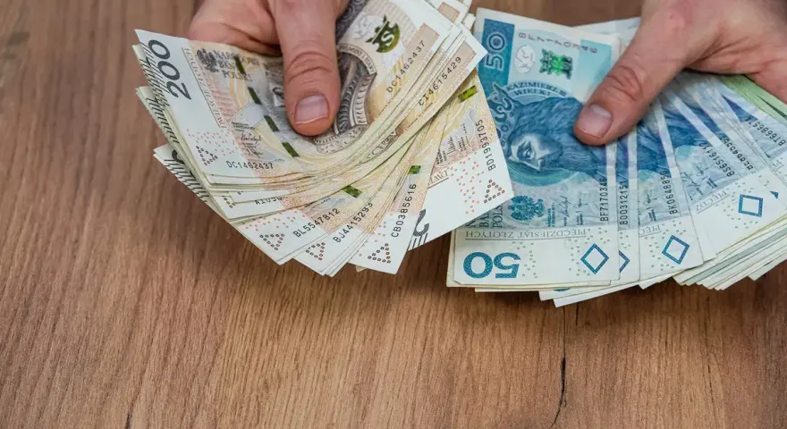 Dłonie trzymające stosy polskich banknotów 200 zł i 50 zł, być może na sześciomiesięczną odprawę emerytalną.